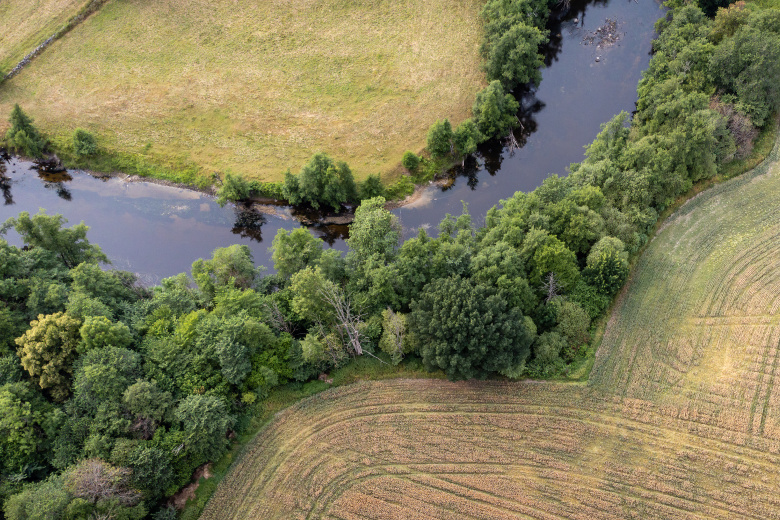 Drönarbild över odlingslandskap med å i mitten. Foto.