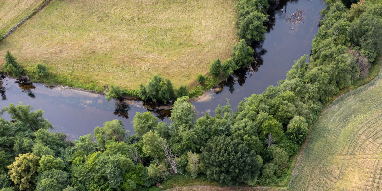 Drönarbild på odlingslandskap med å i mitten. Foto.
