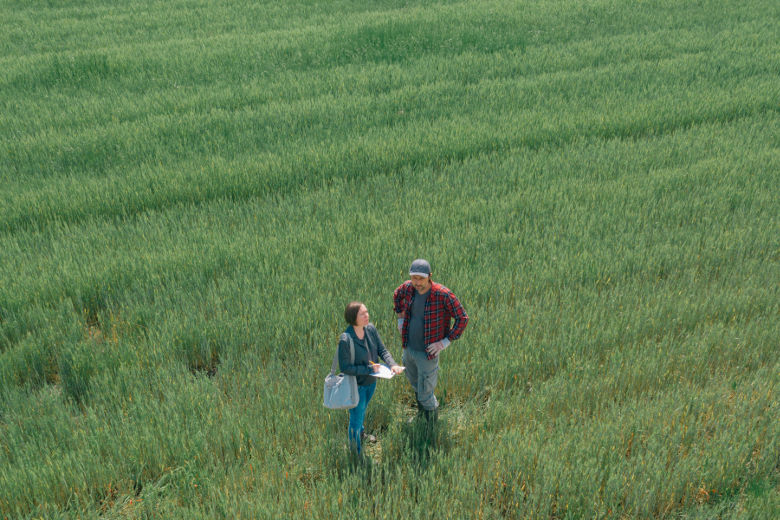 En kvinna med anteckningsblock och en man står tillsammans på ett fält. Foto.